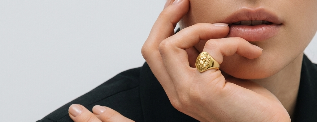 Close-up of a person wearing a gold ring with a lion head design on a plain background